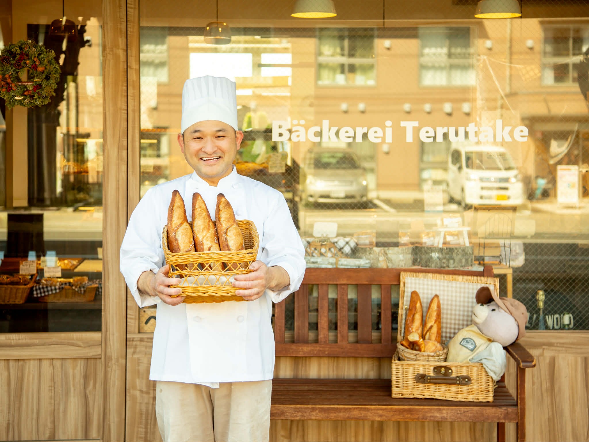 職人・鳥飼がバゲットを抱えて微笑む様子 — Bäckerei Terutake ベッカライテルタケの想いページへ